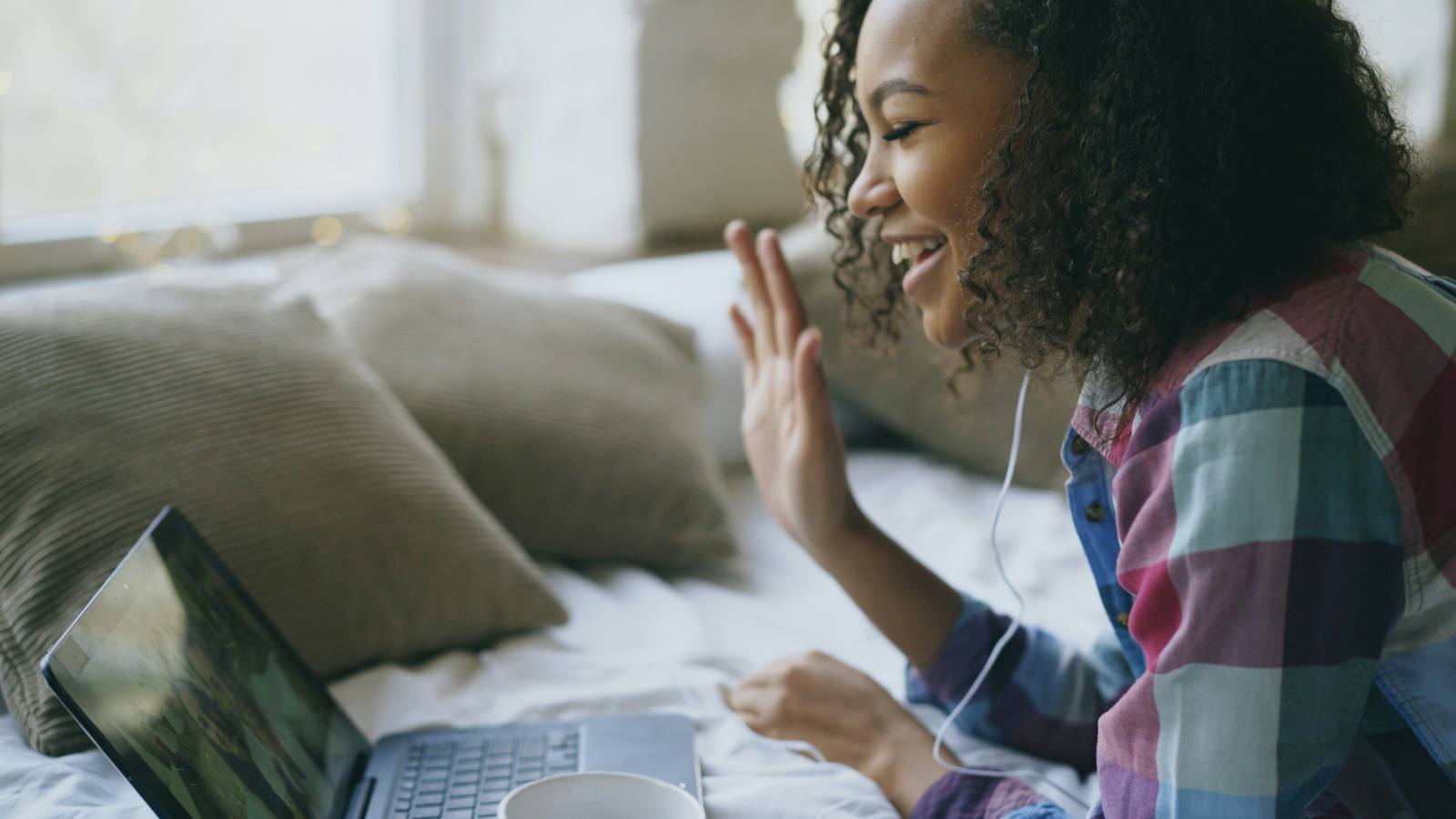 Online English teacher waving to her student on a video call from home