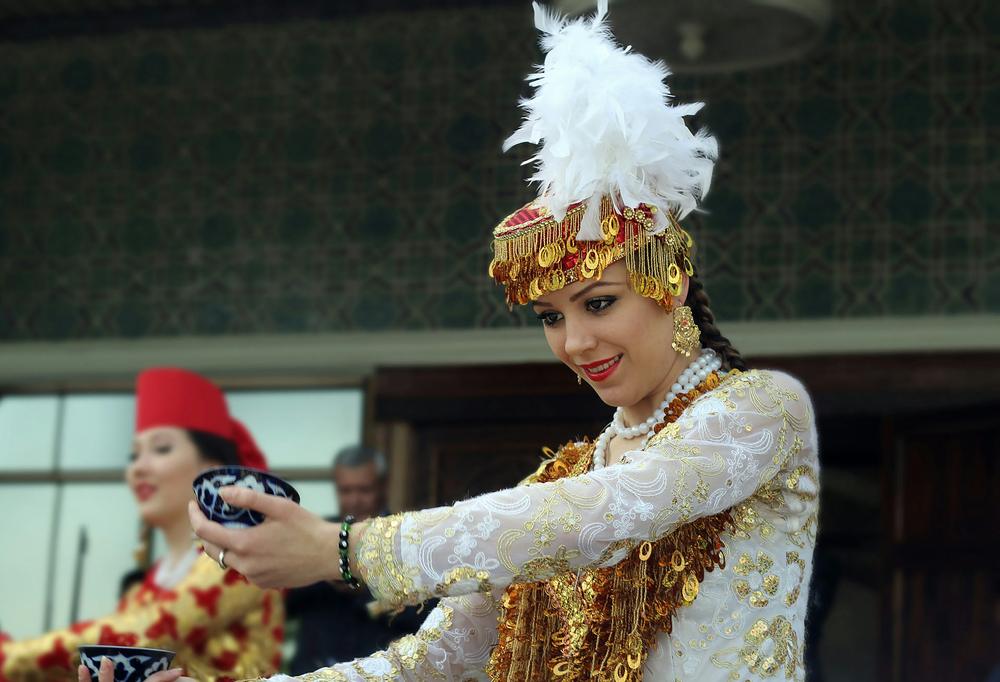 Women in traditional Uzbek dress offering tea, a symbol of Uzbek hospitality